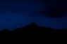 the silhouette of a mountain against a dark blue sky