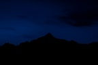 the silhouette of a mountain against a dark blue sky