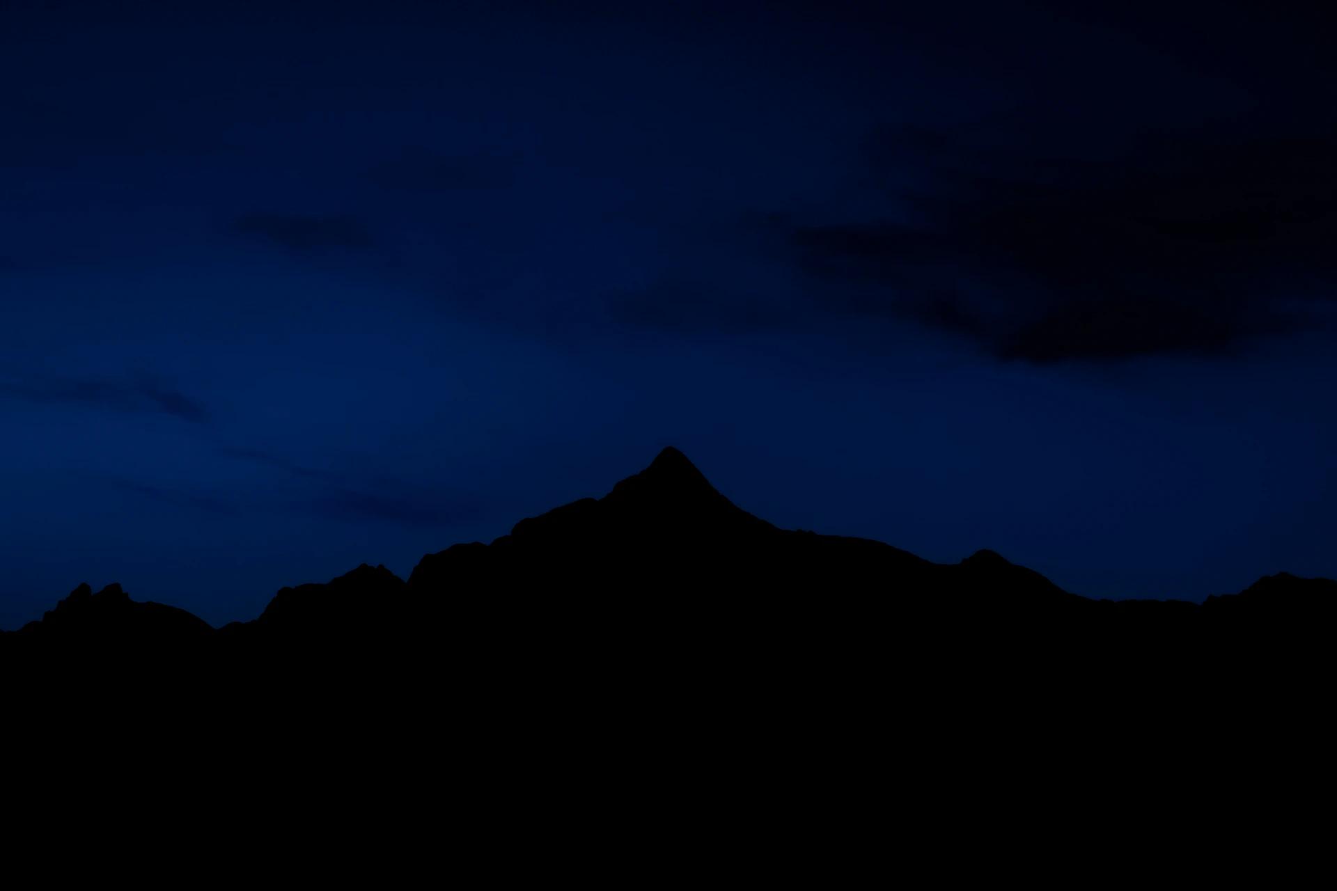 the silhouette of a mountain against a dark blue sky