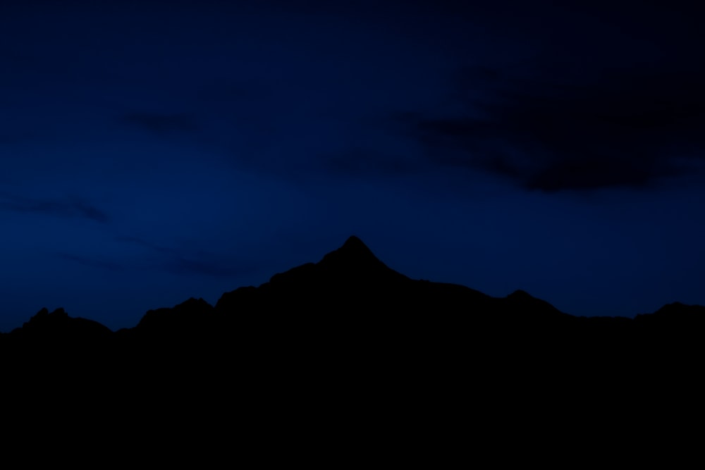 the silhouette of a mountain against a dark blue sky