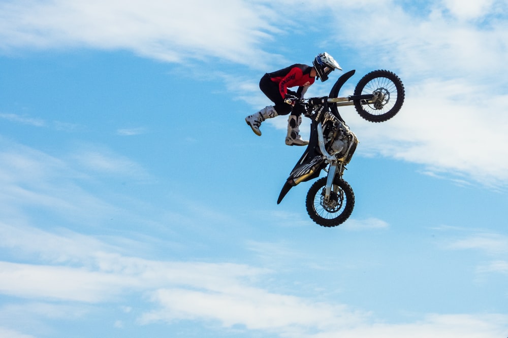 Persona que viste chaqueta roja y negra mientras sostiene una moto de cross de motocross