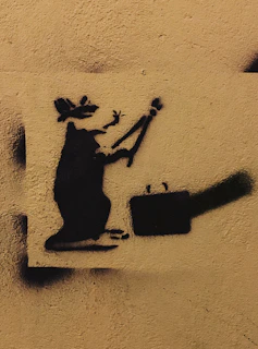A striking Banksy piece depicting a rat holding a paintbrush on an urban alleyway door