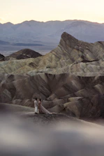 A warm, cinematic photo of Bruce and Gaynor Richter standing together outdoors with mountains in the background, bathed in natural light.