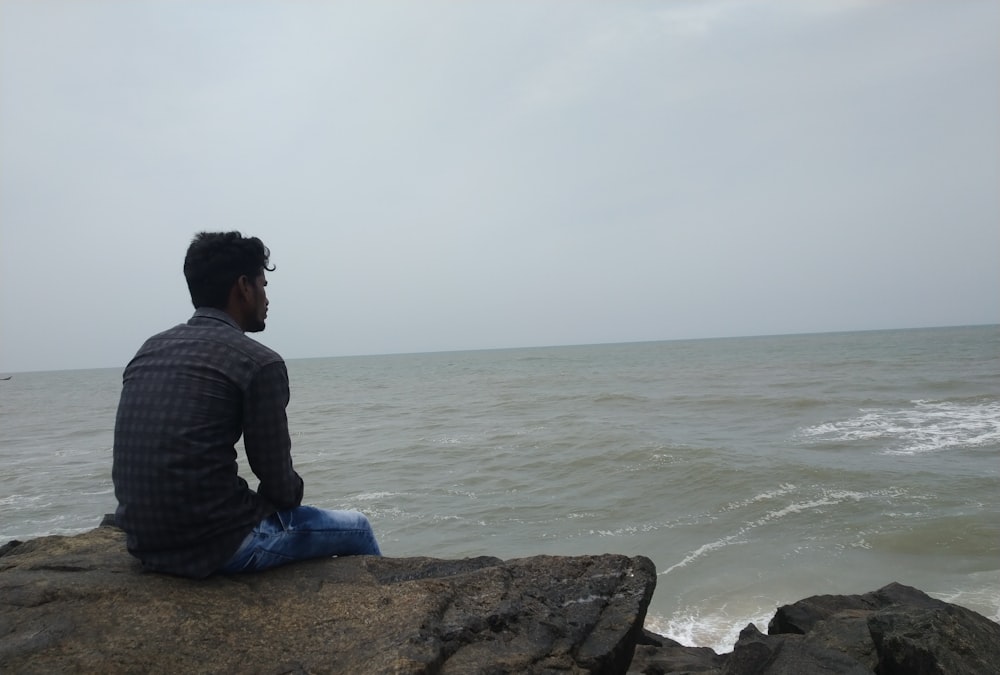 men sitting in a rock near body of water during daytime