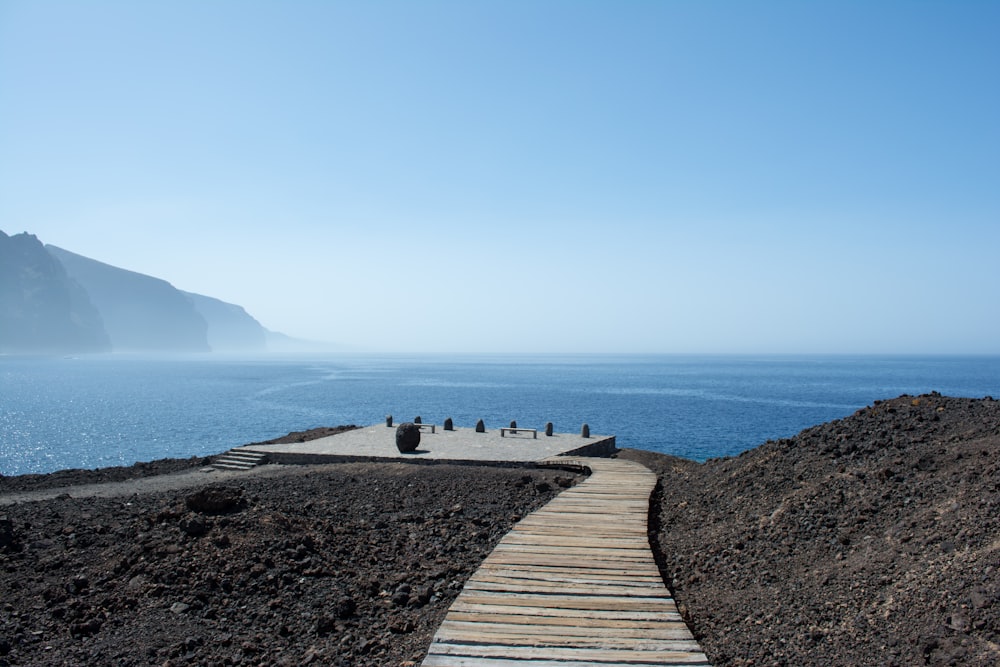 white wooden pathway near body of water under blue sky