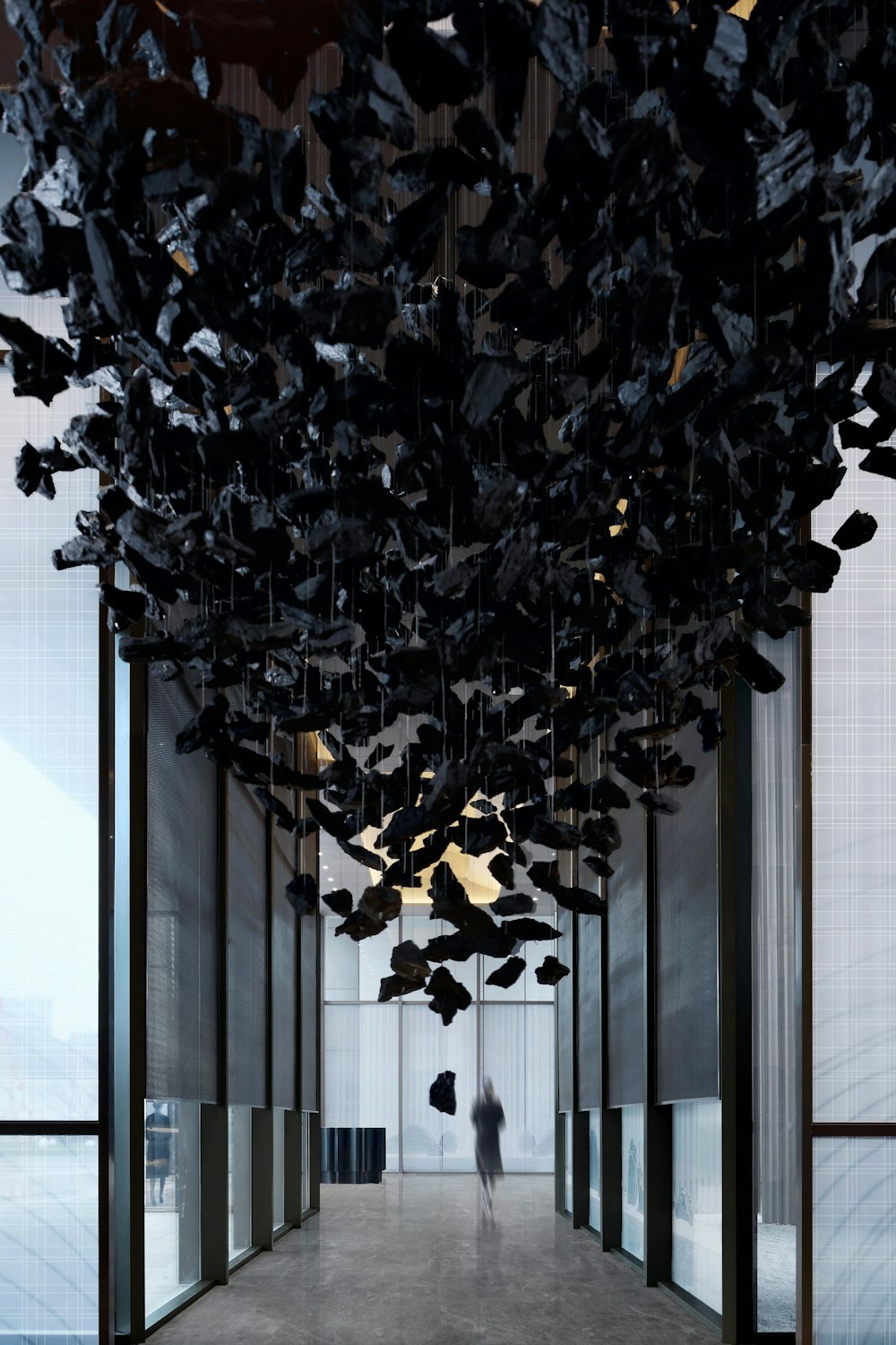 a person walking down a long hallway with lots of black objects hanging from the ceiling