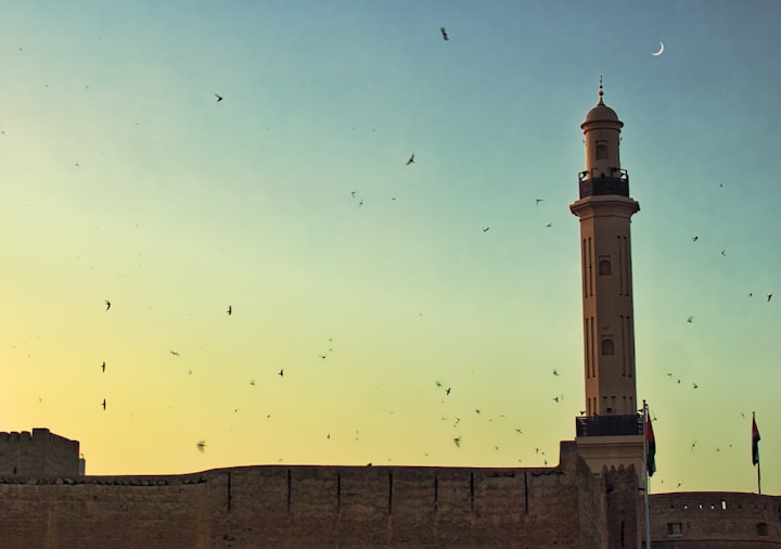 A minaret against an evening sky with birds in the background.