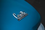 A close-up view of a car's surface displaying the badge with the words 'Corvette Sting Ray' in chrome. The surface is painted in a blue color, with a glossy finish.