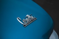 A close-up view of a car's surface displaying the badge with the words 'Corvette Sting Ray' in chrome. The surface is painted in a blue color, with a glossy finish.