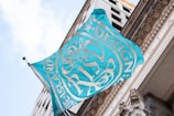 A turquoise and white flag with intricate designs and the text 'Rhode Island School of Design' in white waves in front of a classical building facade.
