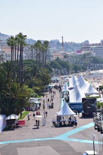 The market path lined with neutral-toned tents, winding under tall palm trees on a bright morning.