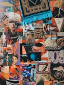 A vibrant collage features a mix of retro and eclectic elements, including vintage posters, illustrations, and various cutouts. There are images of planets, a tapestry with fringe, a white cat, and a dangling toy skeleton. Other items include heart-shaped objects, comic-style art, and old advertisements.