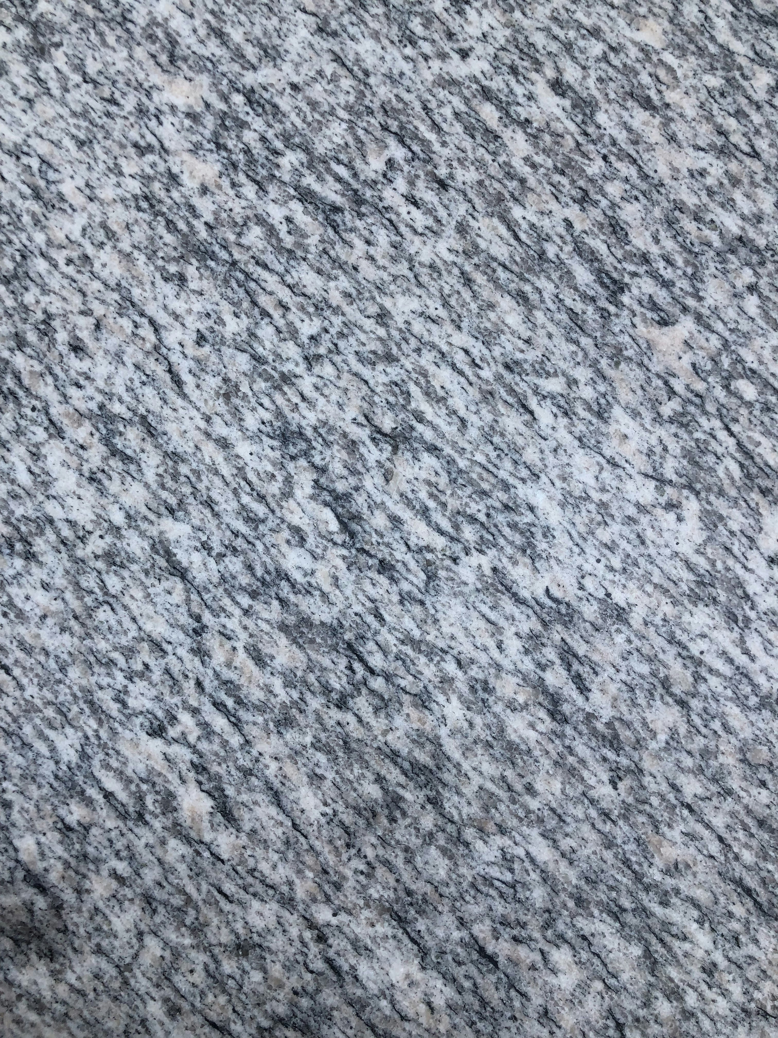 A textured surface with a pattern of interwoven gray, white, and speckled black colors, resembling granite or a similar stone material.
