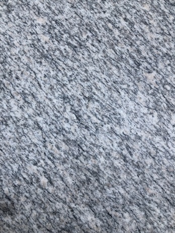 A textured surface with a pattern of interwoven gray, white, and speckled black colors, resembling granite or a similar stone material.