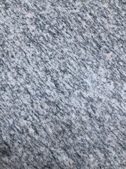 A textured surface with a pattern of interwoven gray, white, and speckled black colors, resembling granite or a similar stone material.