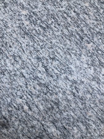 A textured surface with a pattern of interwoven gray, white, and speckled black colors, resembling granite or a similar stone material.
