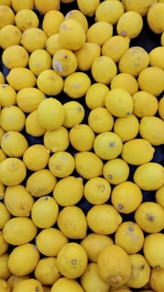 A large collection of bright yellow lemons is densely packed together. Some lemons have slight blemishes or darker spots on their surface.
