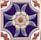 A decorative ceramic tile features a stylized floral design. At the center, a flower with a circular orange core is surrounded by pale yellow and beige petals. Green leaves extend from the flower on a dark blue background. The corners of the tile have additional floral motifs in orange and white.