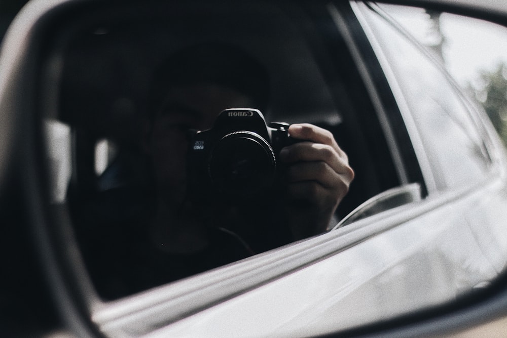reflection of person holding camera on side mirror