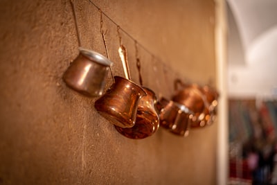 brass-colored cook ware hangs on wall casserole teams background