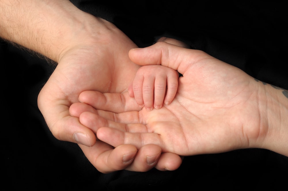 Close-up small hands of baby is lying in men of his father hands, concept  of caring, fatherhood Stock Photo