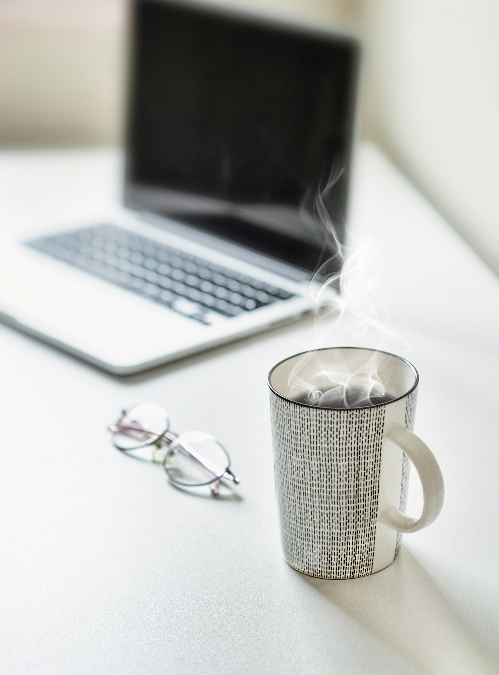 filled cup near eyeglasses and MacBook