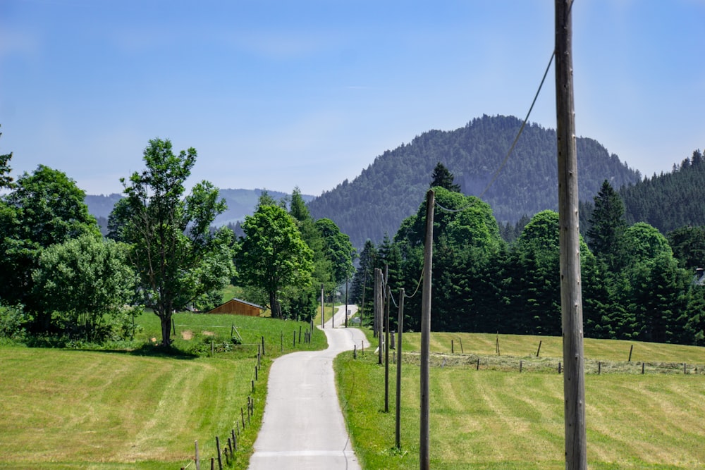 gray concrete road near green field viewing mountain under blue and white skies