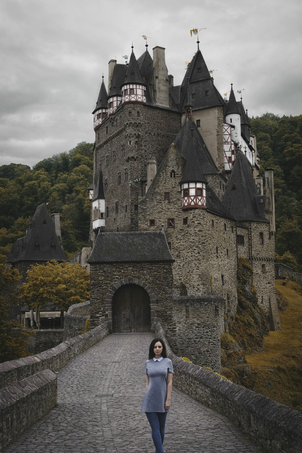 Frau, die in der Nähe der grauen alten Burg spazieren geht, die von hohen und grünen Bäumen umgeben ist