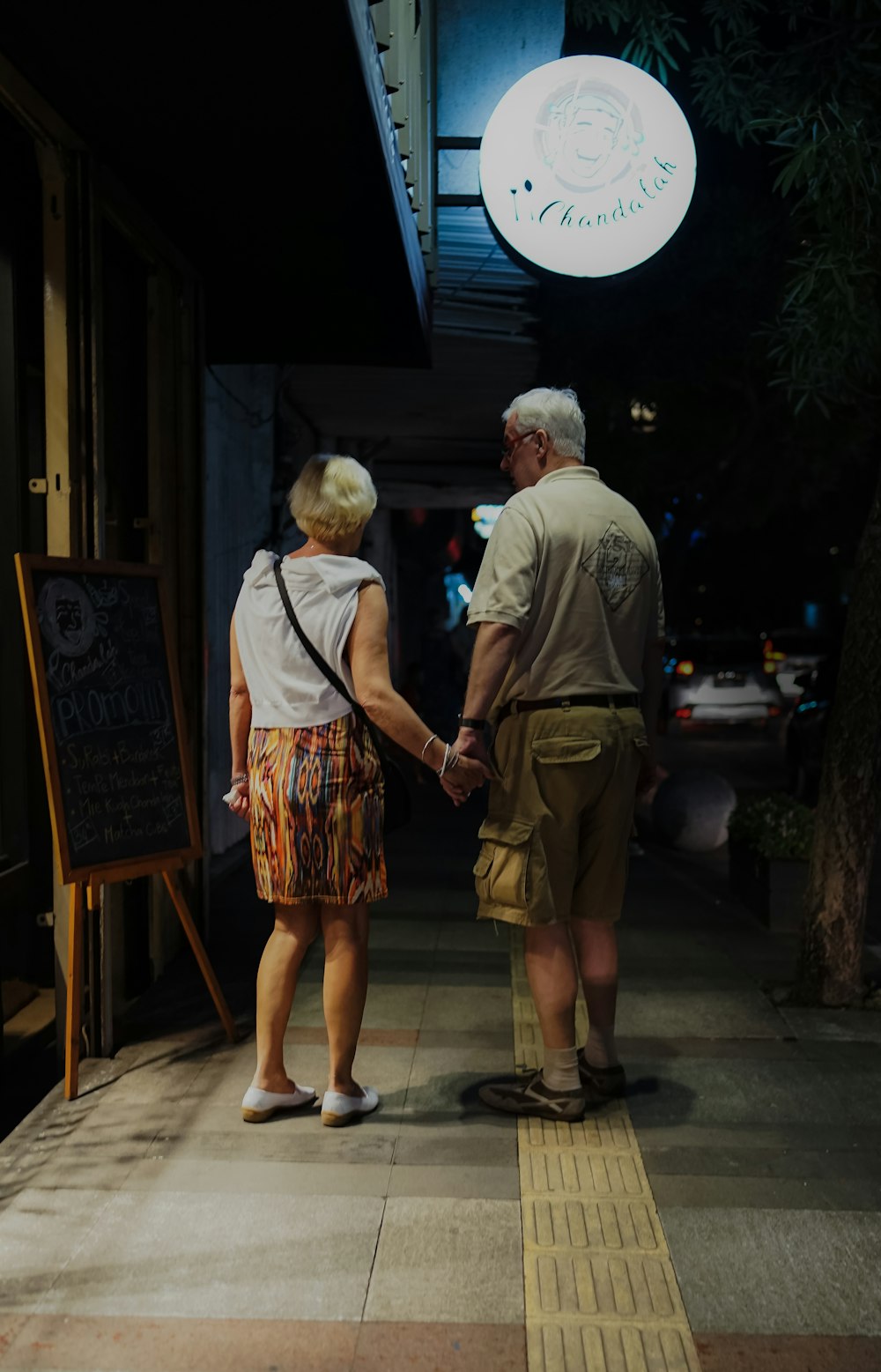 man and woman holding hands standing in front of sign