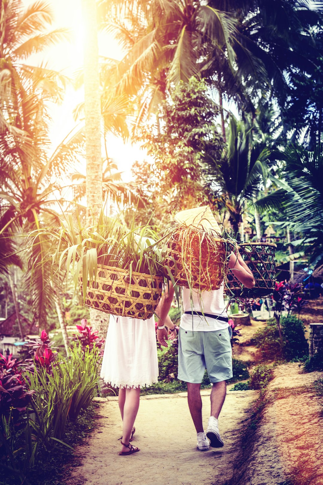 man and woman walking and carrying basket walking on pathway surrounded with plants and trees