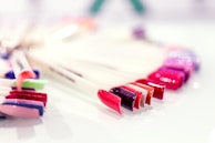 A selection of colorful nail polish samples displayed on a white surface. The colors include shades of red, pink, purple, and metallic tones, arranged neatly in a fan-like formation.