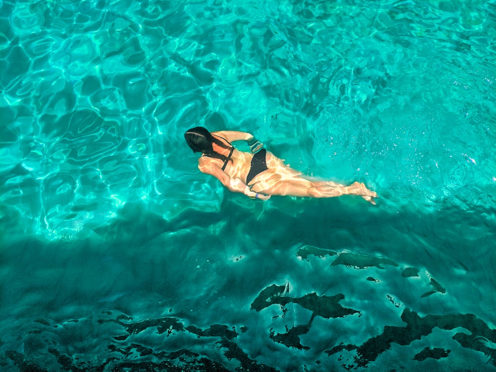 澄んだ青い水の上を泳ぐ黒いビキニの女性