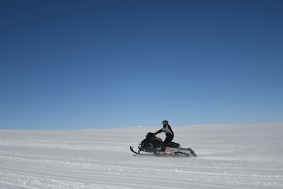 A snowmobile speeding through a snowy landscape under a clear blue sky.
