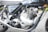 The image features a close-up view of a classic motorcycle engine with detailed components. The metallic engine parts, including the cylinder and exhaust pipes, are prominently visible. The black and silver design is complemented by shiny chrome finishes. The model name '750 Commando' is visible on the bike's side panel.