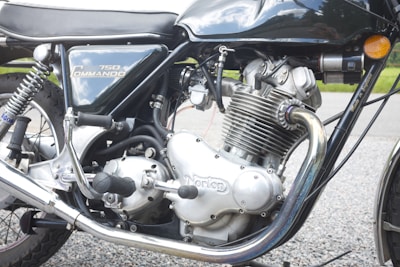 The image features a close-up view of a classic motorcycle engine with detailed components. The metallic engine parts, including the cylinder and exhaust pipes, are prominently visible. The black and silver design is complemented by shiny chrome finishes. The model name '750 Commando' is visible on the bike's side panel.