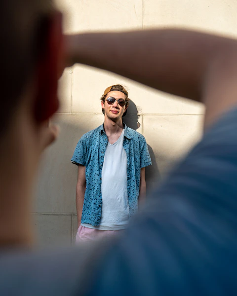 Over-the-shoulder framing — out-of-focus shoulder and hand in foreground, sharp subject (man with sunglasses) in background