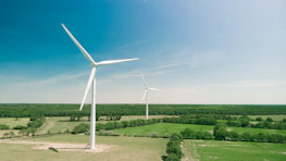 A vibrant green landscape with solar panels and wind turbines under a clear sky.