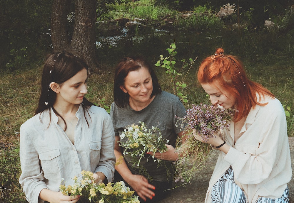 three women holding bouquet of flowers while one of them sniffing the flowers