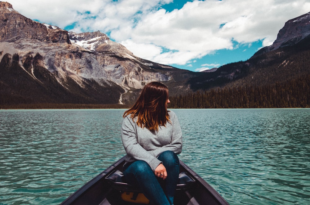 Femme en pull gris assise sur un bateau et regardant sur son côté gauche