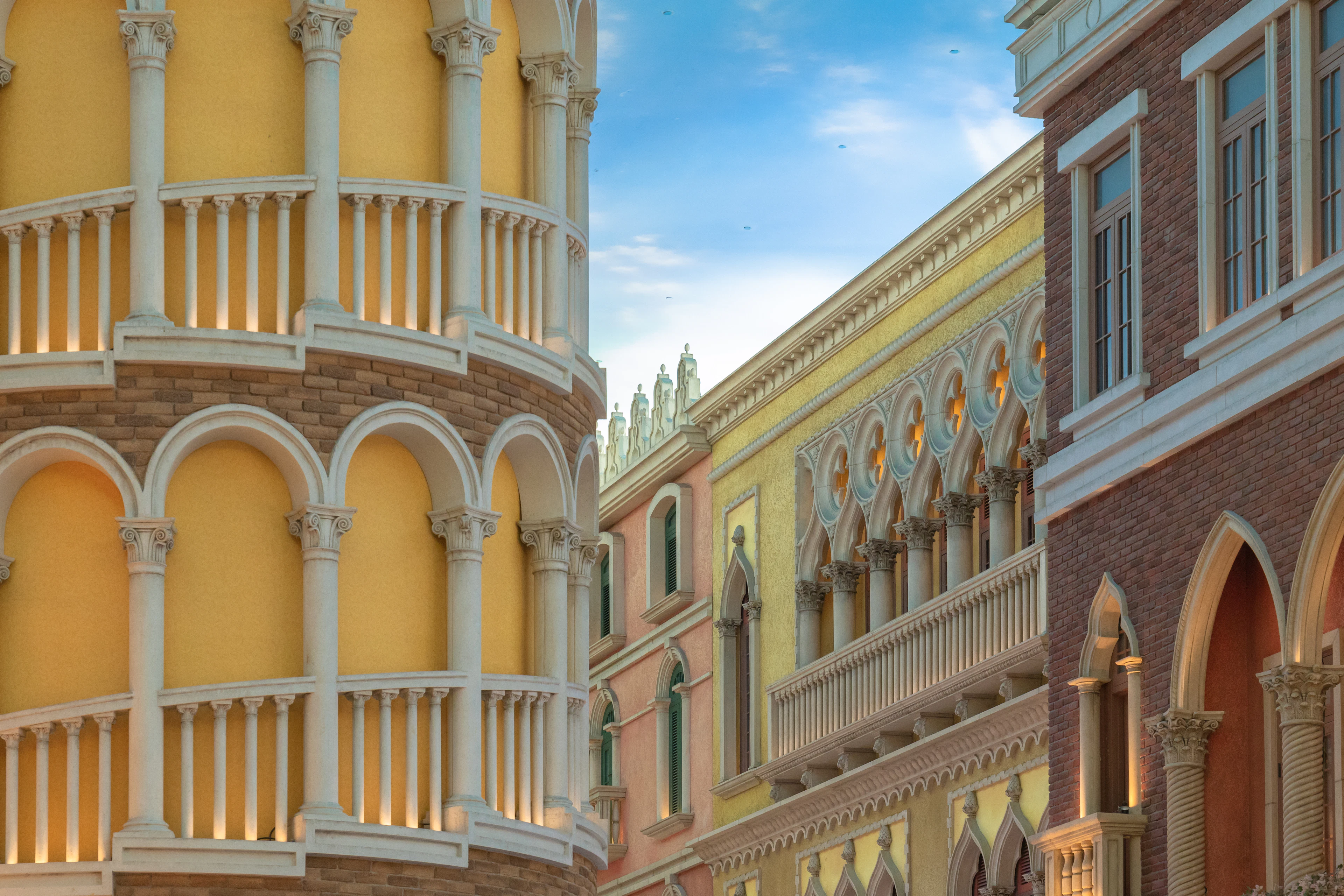 The ochre and rose Venetian-style facades of the Venetian Macao resort in Cotai, tiers of white arcades and balustrades layered against a blue sky in late afternoon light.
