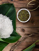 A rustic wooden table laid out with a pack of moongcraft, raw moong dal, and fresh lime green leaves