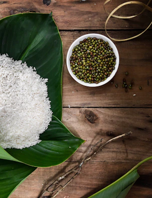 A rustic wooden table laid out with a pack of moongcraft, raw moong dal, and fresh lime green leaves