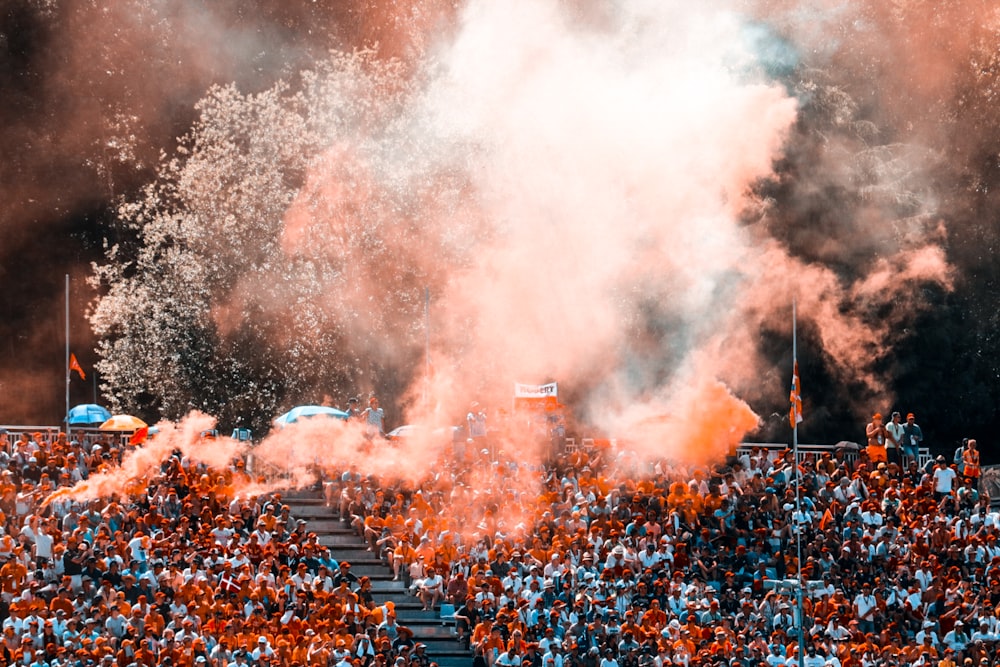 aerial photo of people sitting on stadium with orange smokes above them