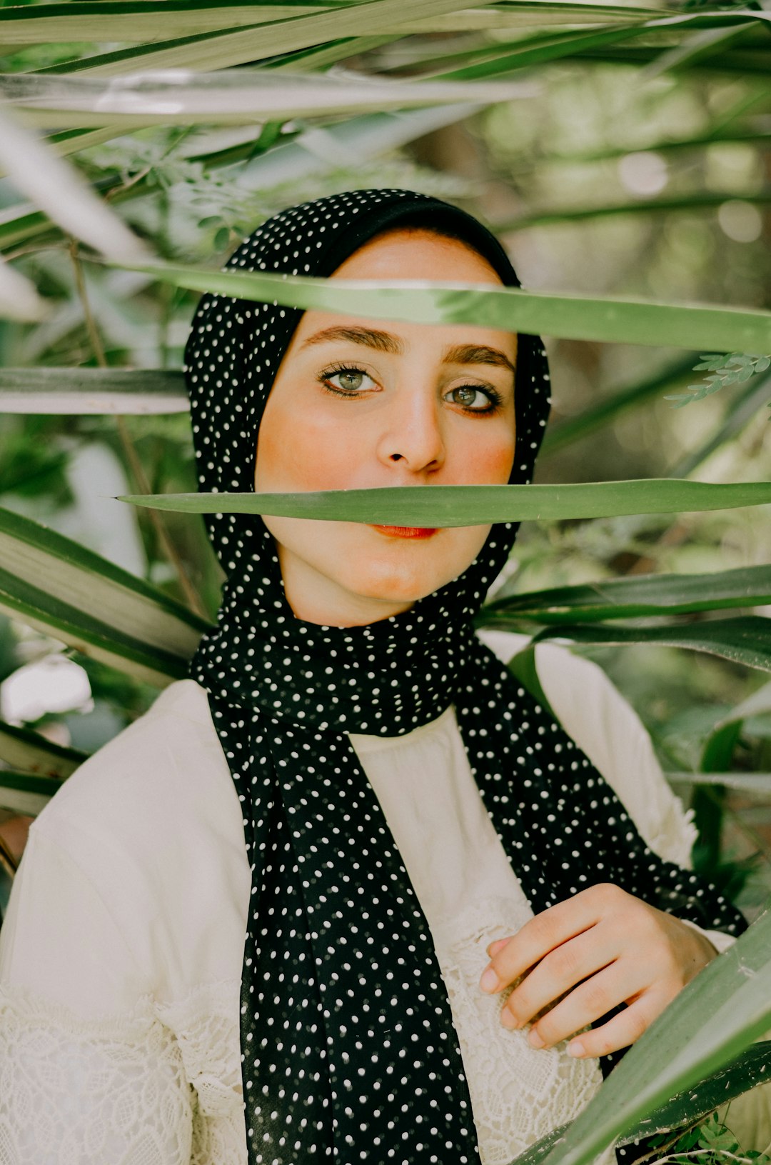 woman wearing black and white spotted hijab standing beside palm plants