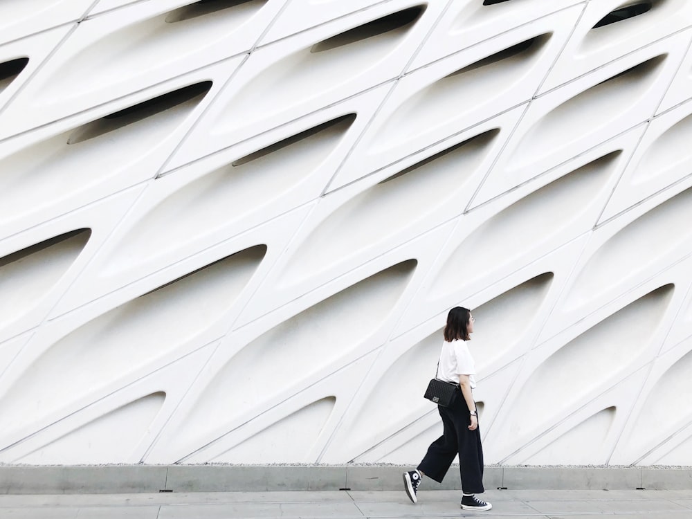 woman wearing white top and black pants near wall