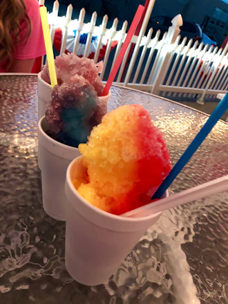 A vibrant frozen cup with colorful layers and sprinkles, surrounded by happy kids at a sunny outdoor party.