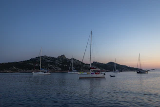 A classic sailboat anchored near a rocky coastline at sunset.