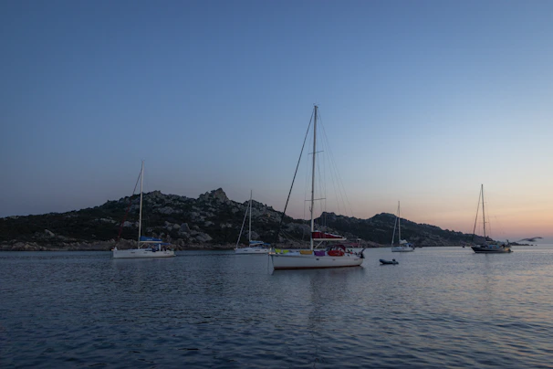 A classic wooden sailboat anchored peacefully near a rocky shoreline at sunset.