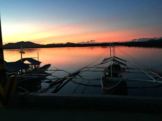 A serene view of a traditional fishing boat gliding through calm lagoon waters at sunset, framed by soft natural greenery.