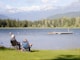 two persons sitting on grass facing the lake